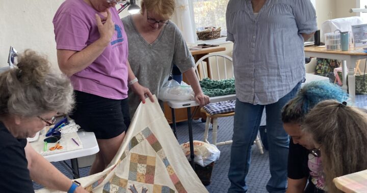 Three ladies examining a quilt.